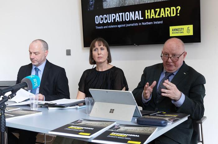 Séamus Dooley, seated next to Kathryn Torney and Patrick Corrigan, speaks in front of a banner displaying the words 'Occupational Hazard?'