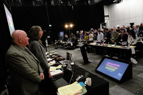 Delegates at DM stand at desk for minute's silence.