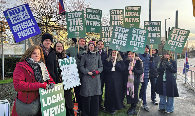 NUJ members stand on a picket line outside STV Glasgow HQ holding green 'Stop The Cuts' and 'Support Local News' placards.