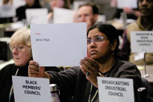 Woman holds sheet with names of journalists killed. other delegates seen in background.