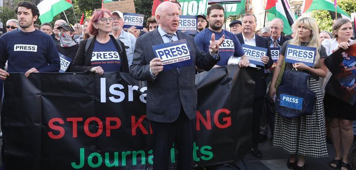 Séamus Dooley, NUJ assistant general secretary, wearing a blazer and tie speaks as people wear 'Press' t-shirts in the background.