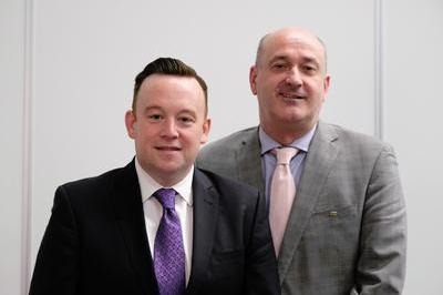 Fran wears a white shirt and dark suit, Gerry wears a grey suit and pink tie.