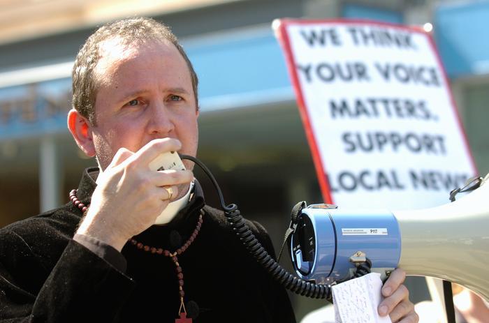 Jonathan Lovett holding a megaphone with an NUJ placard in the background.