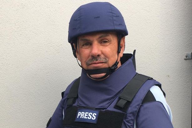 Mick wears a dark blue helmet and dark blue and black vest marked press.