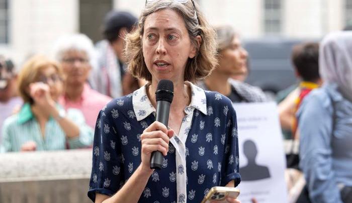 Laura Davison, holding a microphone, speaks in front of Downing Street in front of the press and protestors.