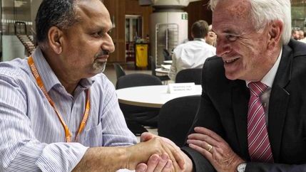 Barnie Choudhury and John McDonnell sitting at a table and shaking hands.