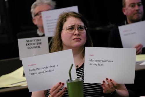 Woman holds two sheets with names of journalists killed. other delegates seen in background.