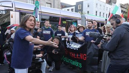 Journalists wearing blue 'Press' t-shirts stand in front of a banner that reads 'Israel, Stop Killing journalists' in central Dublin.
