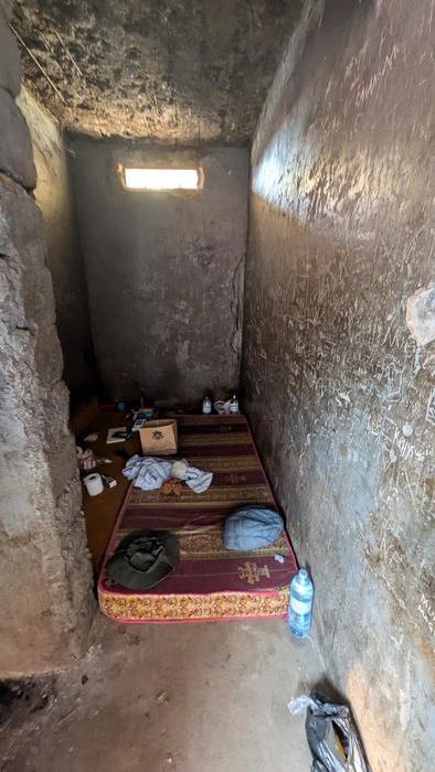 Vertical image of a 2m x 3m cell with a mattress and a small rectangular hole in the wall with light coming through.