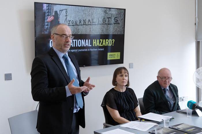 Patrick Corrigan stands in front of a screen displaying the words 'Occupational Hazard?' alongside Kathryn Torney and Séamus Dooley. 