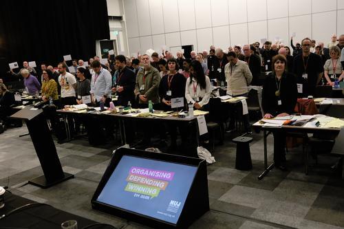 Delegates stand at tables in a moment's silence